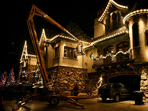 A Christmas light installer uses a lift to hang Christmas lights on this home.